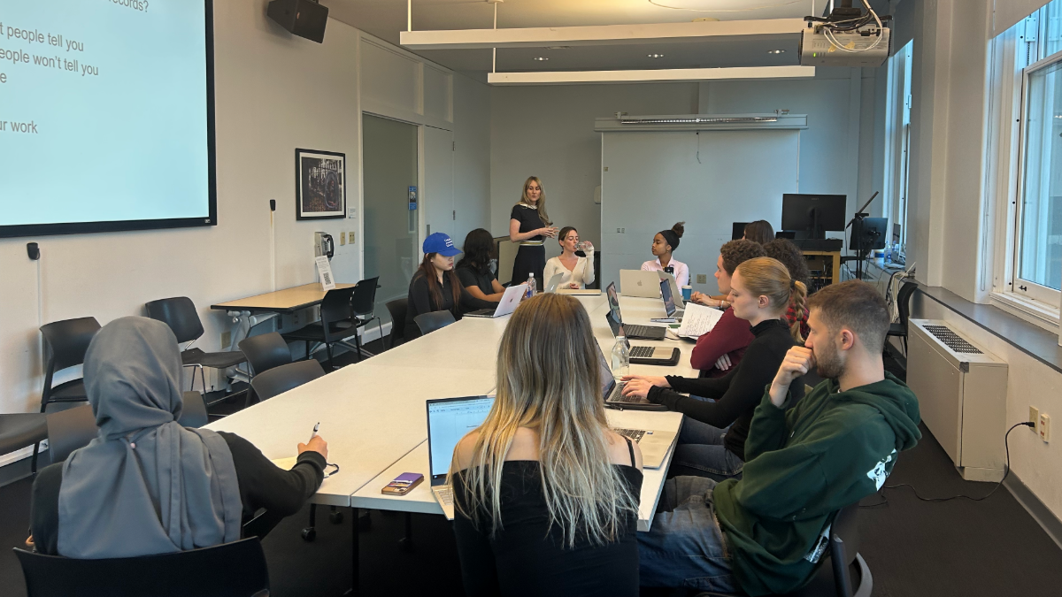 A classroom with students sitting around a large rectangular table. 