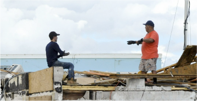 Two workers atop a destroyed roof