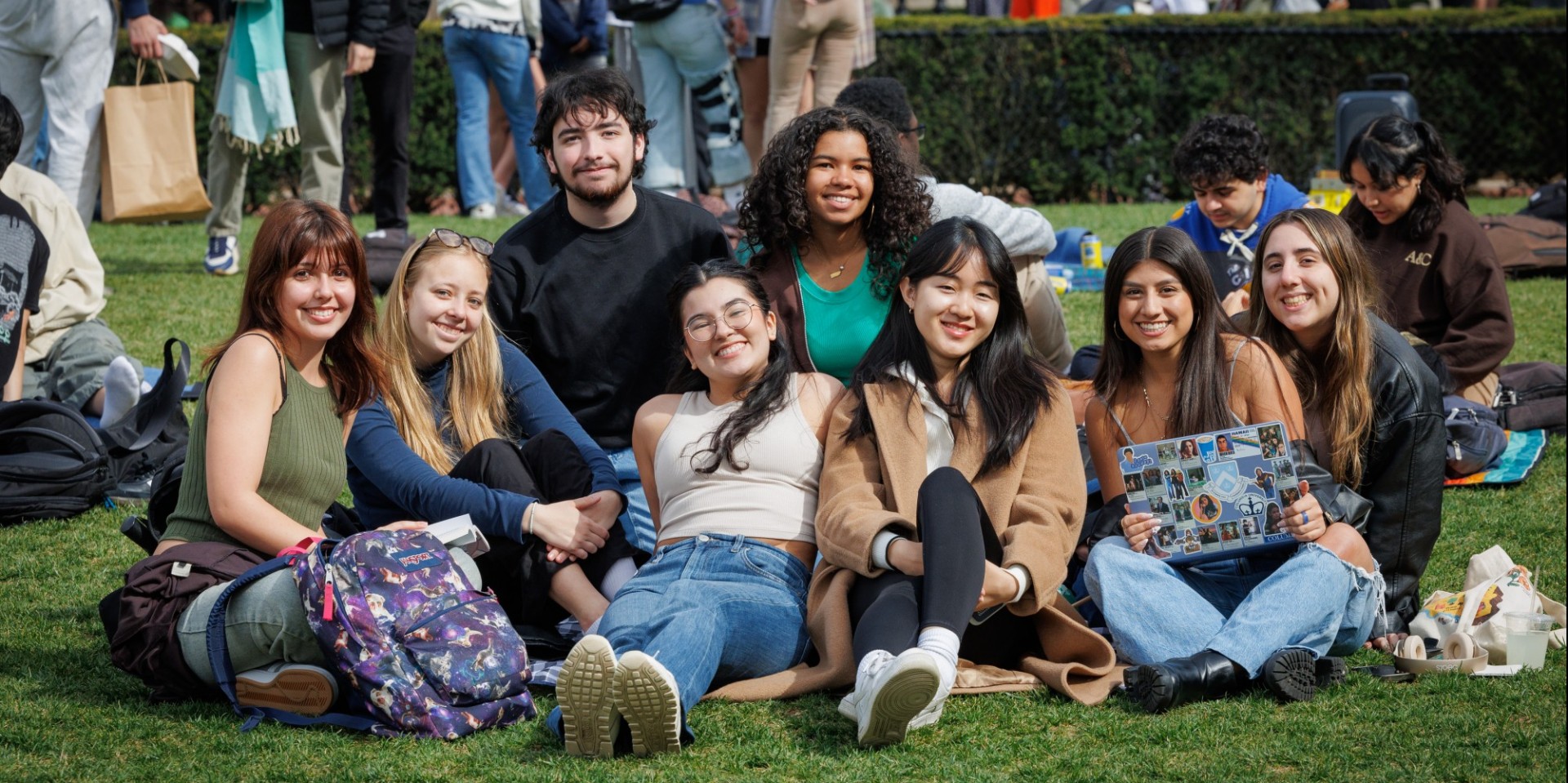 Exterior shot of smiling students sitting in grass, photographed by Sirin Samman in Spring 2024.