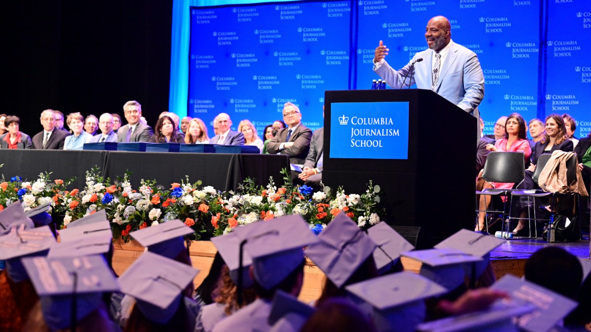 Man speaking at a podium in front of a crowd wearing caps and gowns. 