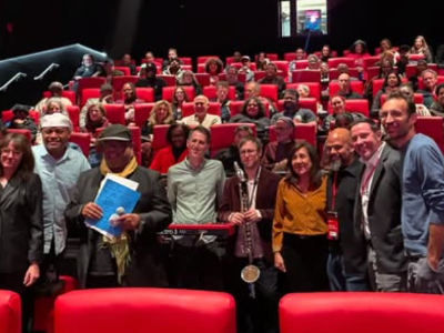 Group photographed in front of a crowded movie theater audience. 