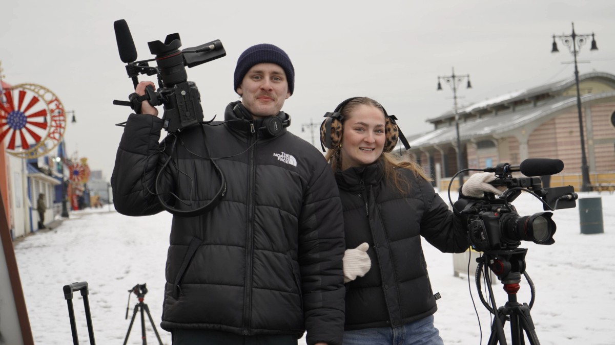 Two students with camera equipment with Coney Island as the backdrop. 