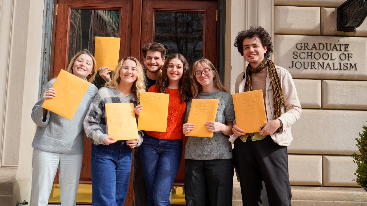 Six students holding yellow folders outside the front door of Pulitzer Hall. 
