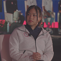A woman being interviewed, speaking into a microphone while seated.