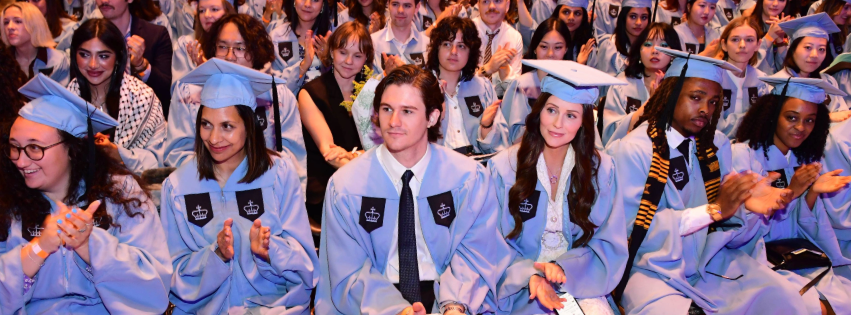 Graduates seated wearing Columbia blue caps and gowns during the Columbia Journalism School Class of 2024 graduation ceremony. 