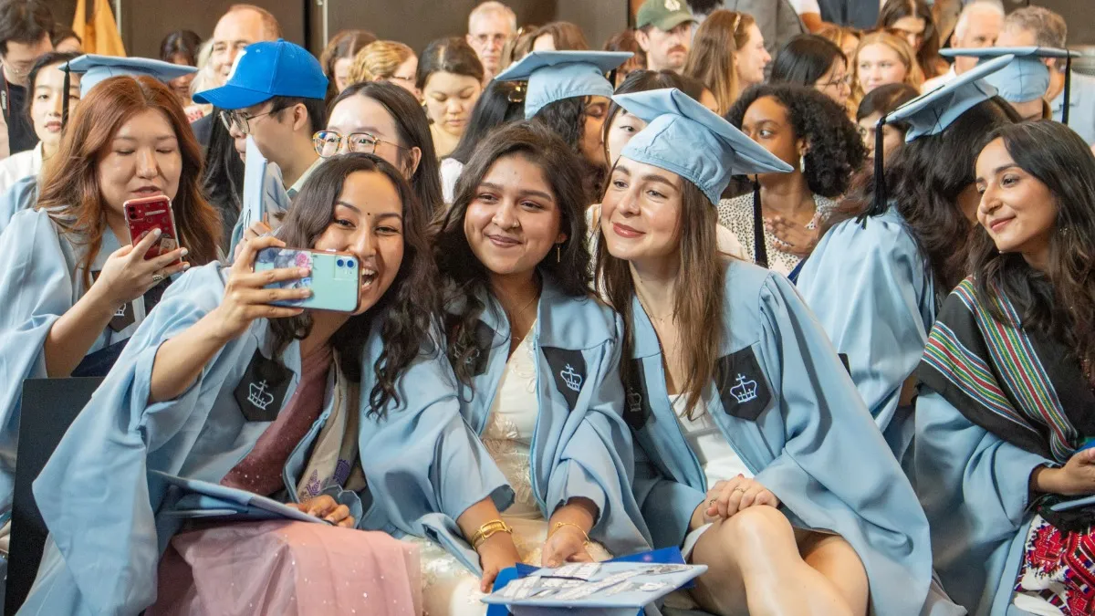 Graduates take a selfie while seated in the audience. 