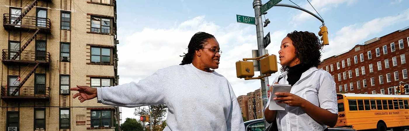 female reporter interviewing a woman while both stand on a sidewalk in the Bronx
