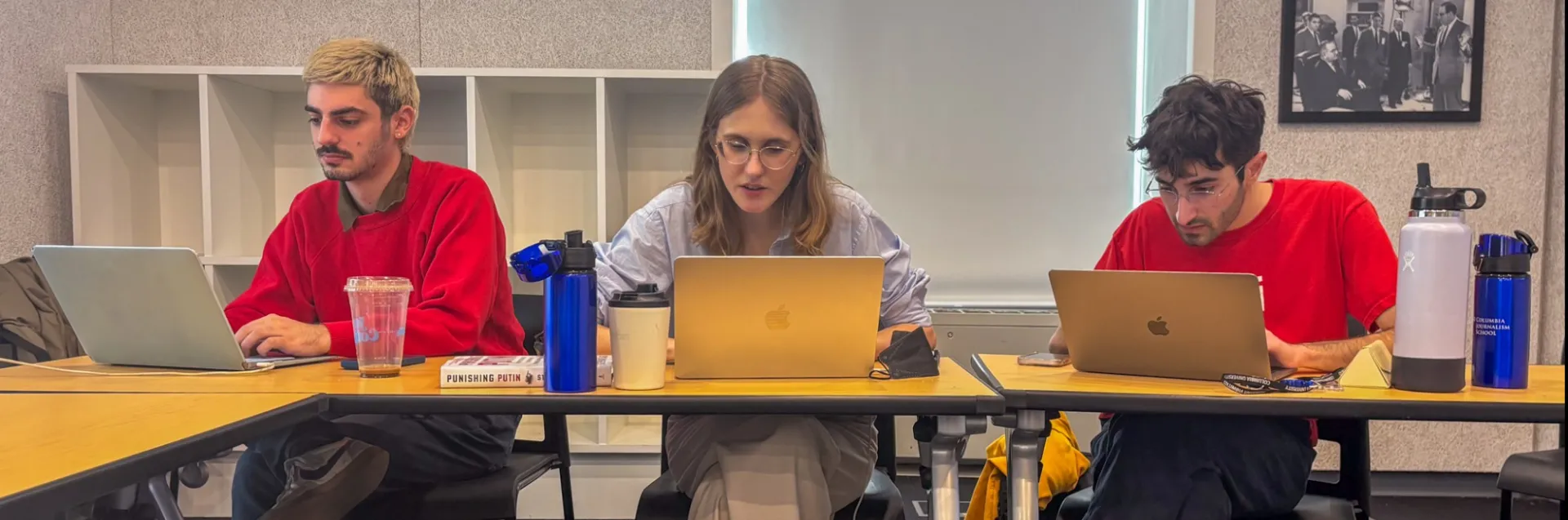 Three students on their laptops in a classroom.