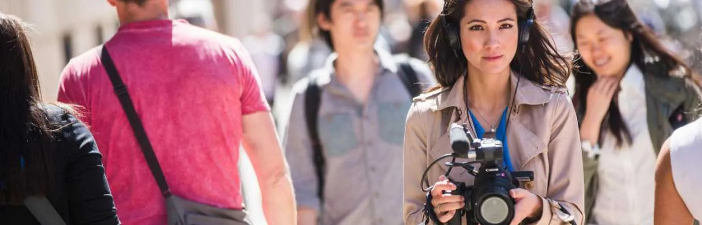 woman walking on busy sidewalk with video camera in her hands