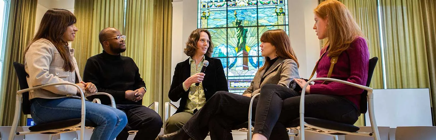 Four women and one man engaged in conversation while seated in tall chairs