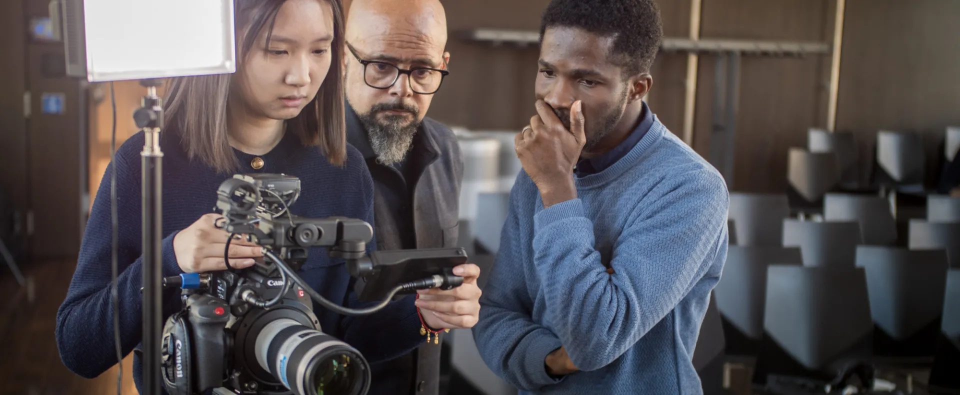 Three people working on a camera setup with empty chairs in the background.