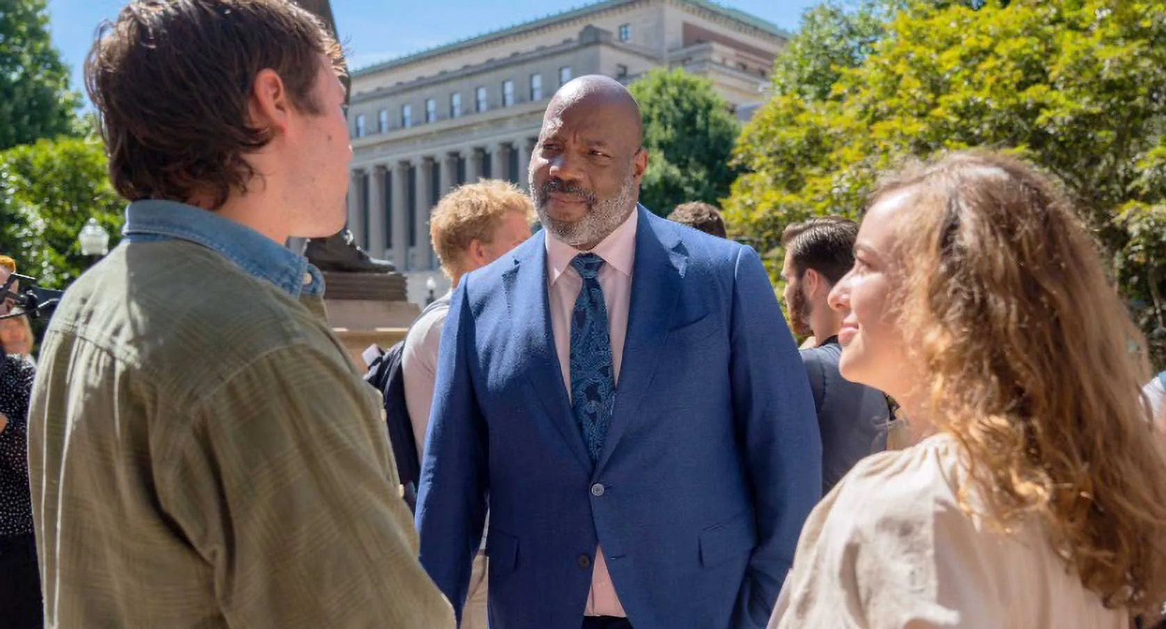 a male and female student talking with a man in wearing a suit