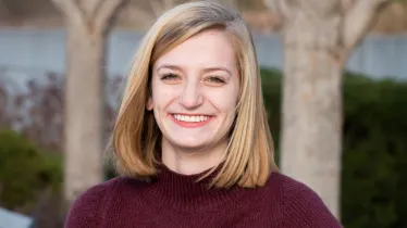 Person with blonde hair smiling, wearing a maroon sweater, outdoors.