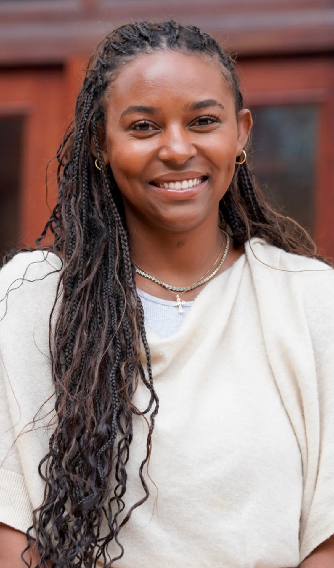 Person smiling with braided hair, wearing a light-colored top and accessories.