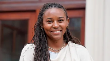 Person smiling with braided hair, wearing a light-colored top and accessories.