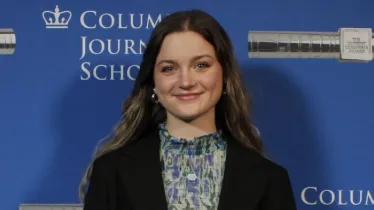 Person standing in front of a blue background with text "Columbia Journalism School."