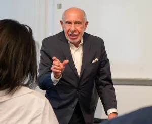 Man wearing a suit speaks to a class. 