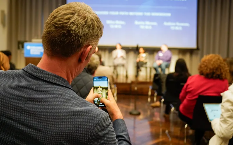 Man taking a photo of a panel on a stage. 
