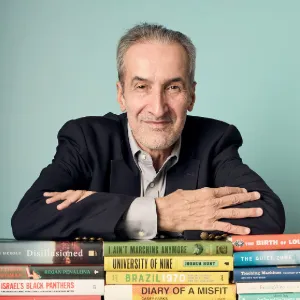 Photo of Sam Freedman with a stack of books. 