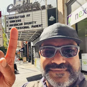 Man taking a selfie pointing up to a movie theater marquee. 