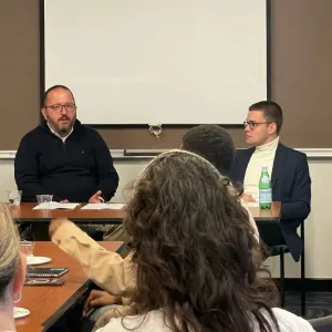 A two-person panel sits in the front of a classroom. 