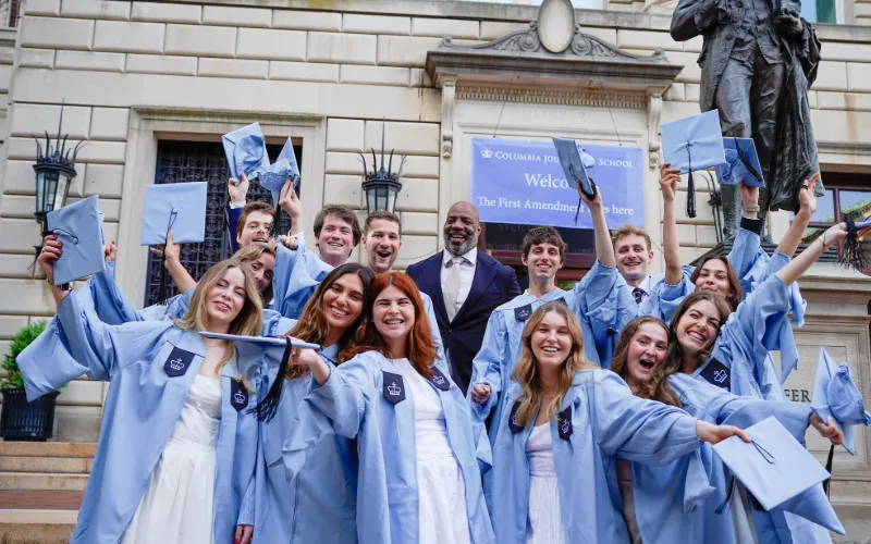 Group of graduates joyfully poses for a photo outside of Pulitzer Hall. 