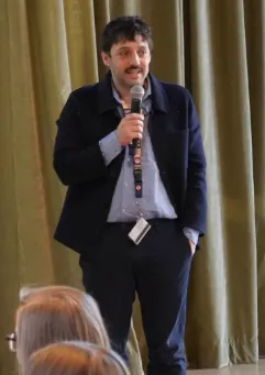 Sacha Biazzo, '24 M.A. Politics, standing and speaking to a microphone