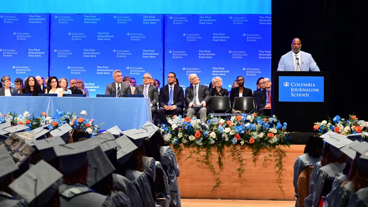 A man addresses a crowd of graduates wearing caps and gowns.