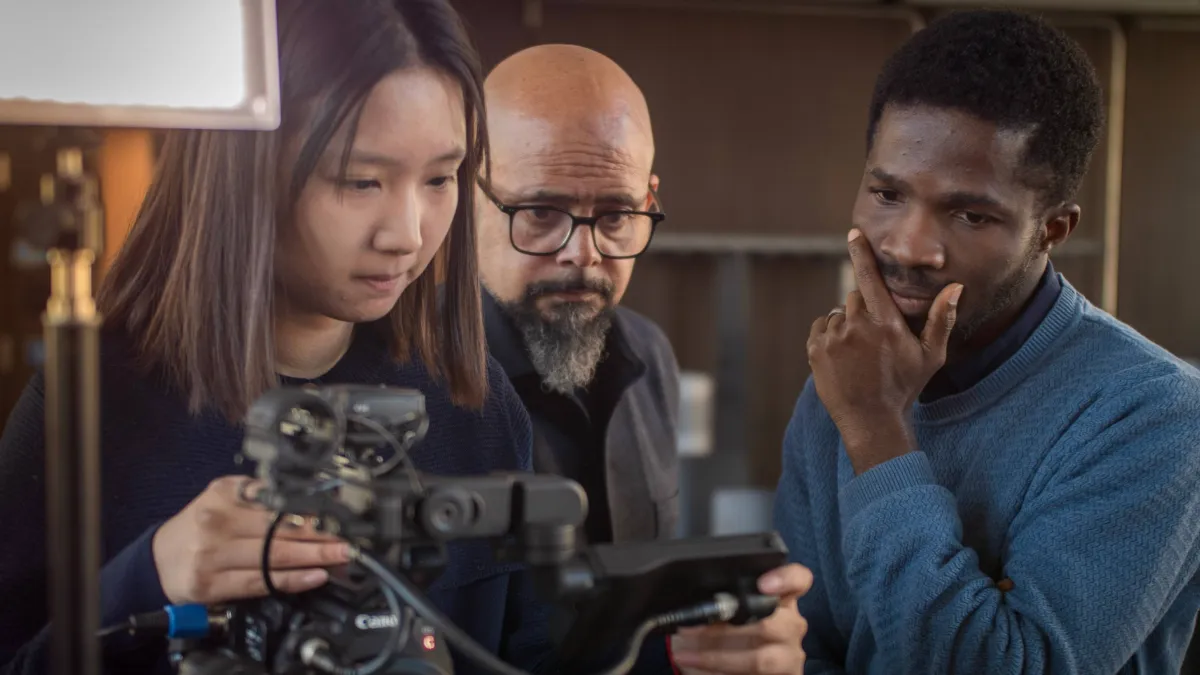 Three people looking at the display of a video camera. 