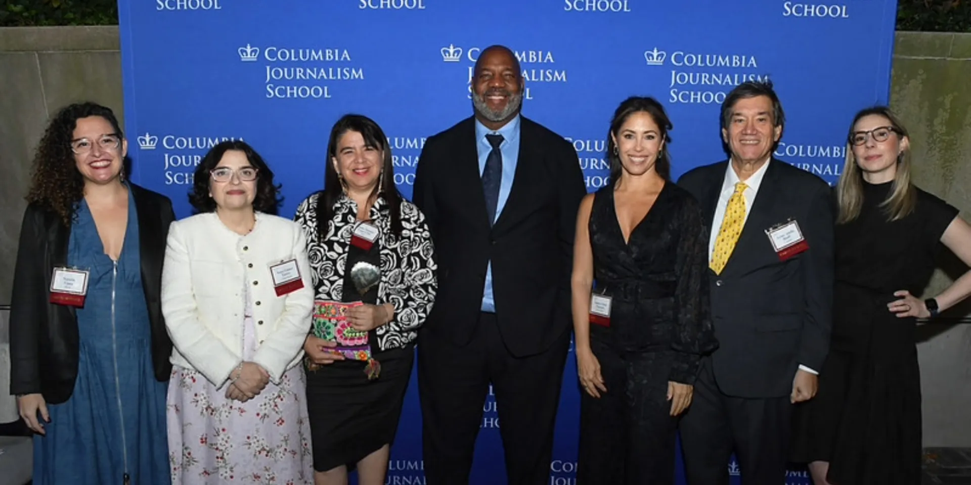 A group of seven people on a red carpet in front of a "Columbia Journalism School" backdrop.