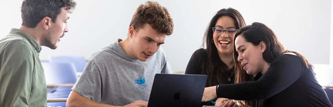 Photo of two male and two female students working together around a laptop, having a laugh