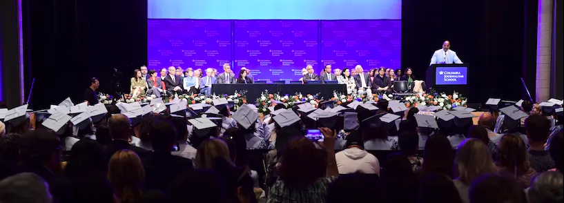 Students in caps and gowns face a stage. 