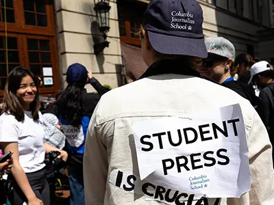 Columbia Journalism student facing away from camera with a sign taped to the back of their shirt that reads, "Student Press, Columbia Journalism School." 
