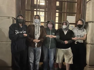 Photo of students linking arms in front of academic building.