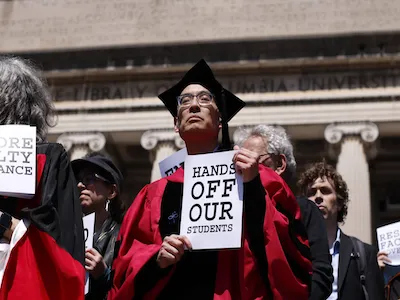 Photo of Columbia faculty member during protest holding sign that reads, "Hands off our students."