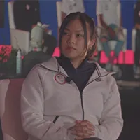 A woman being interviewed, speaking into a microphone while seated. 