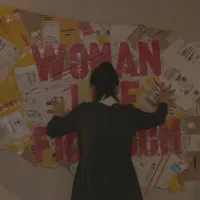 An artist places a collaged map of America with bolded red words overtop it on a blank wall. 