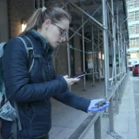 A woman wearing a backpack takes a photo of an injured bird on the streets of New York. 