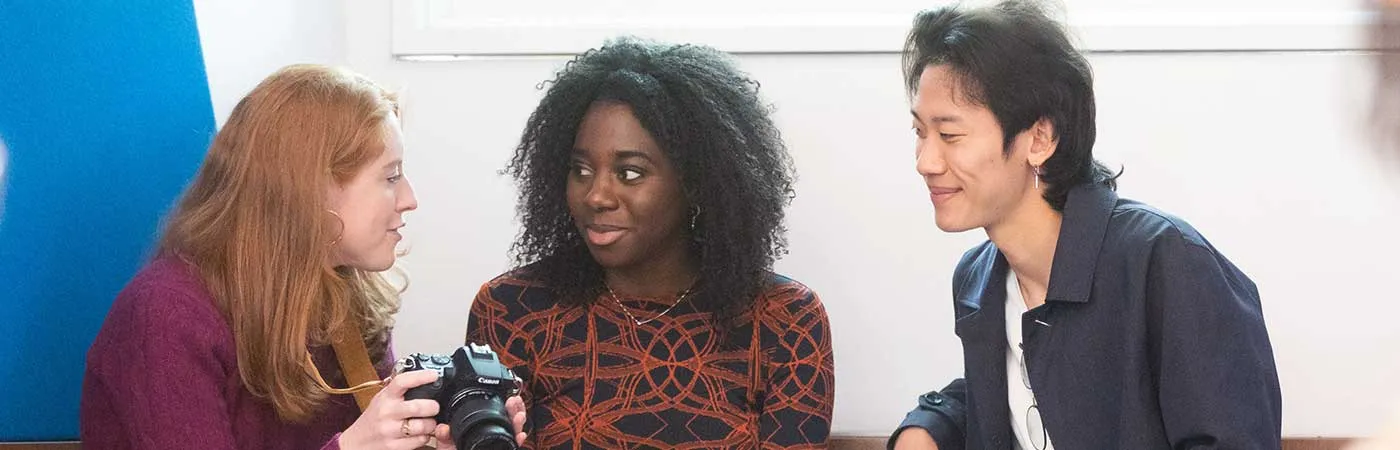 three students in conversation, one holding a camera
