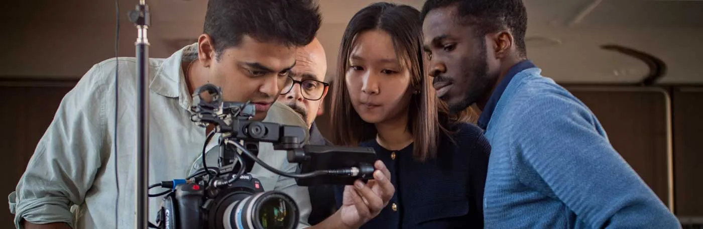 three students with a professor lining up a shot using a video camera in studio