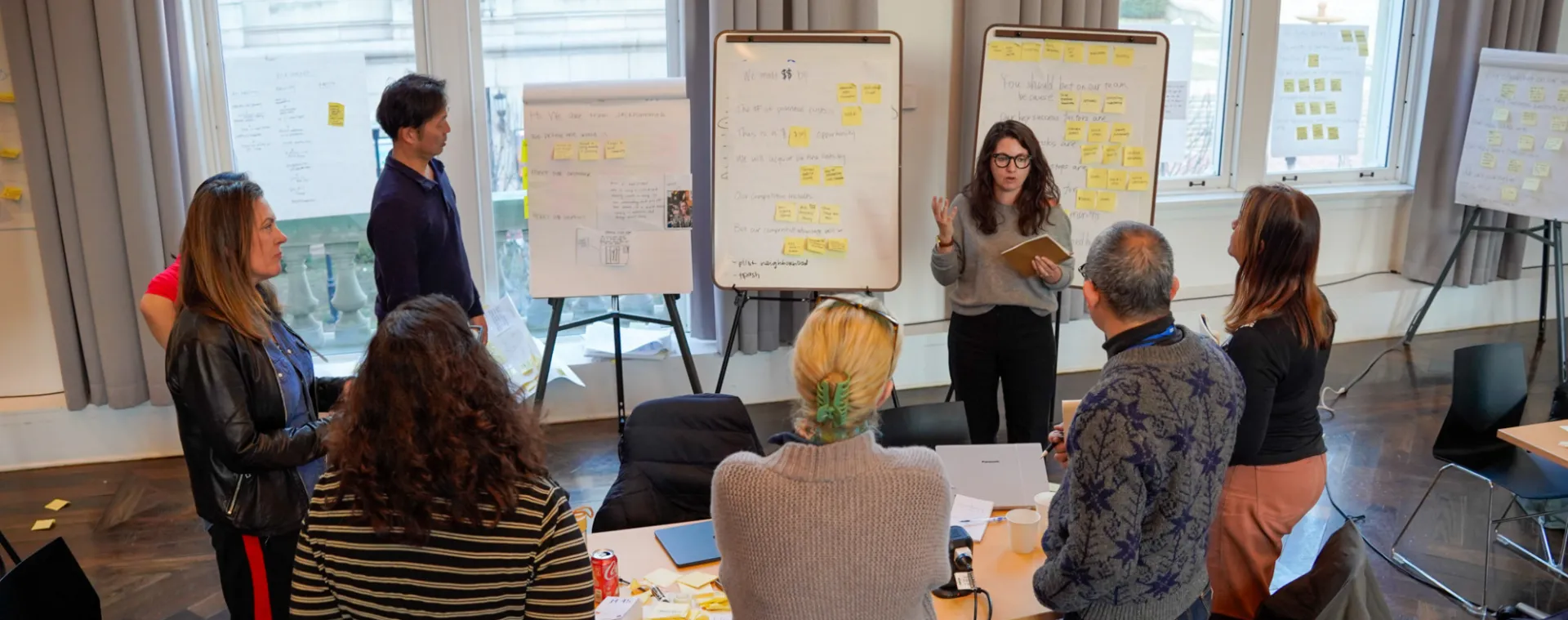 Woman presenting near a whiteboard with sticky notes and text.