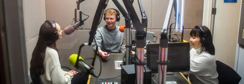 Three students in a podcast recording booth. 