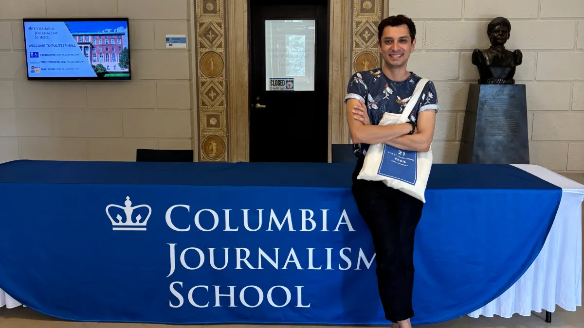 Photo of Neville Bhandara in front of a table featuring the CJS logo. 