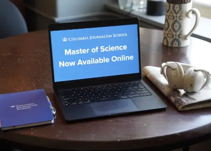 Laptop displaying a Columbia Journalism School announcement for an online Master of Science program, surrounded by a notebook and headphones. 