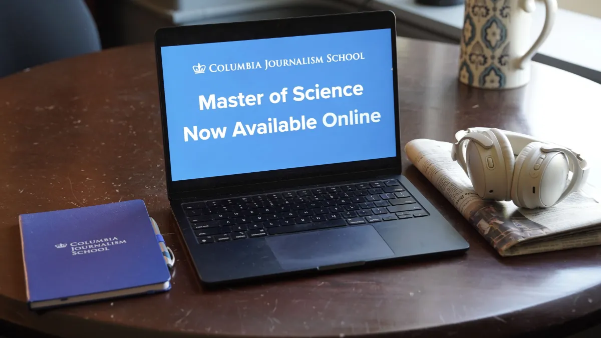 Laptop displaying a Columbia Journalism School announcement for an online Master of Science program, surrounded by a notebook and headphones. 
