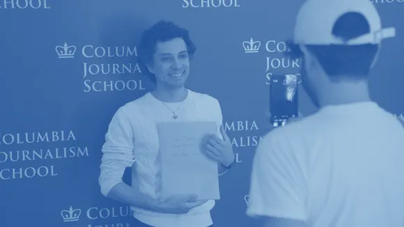 Student in front of a banner with the Columbia Journalism School logo. 