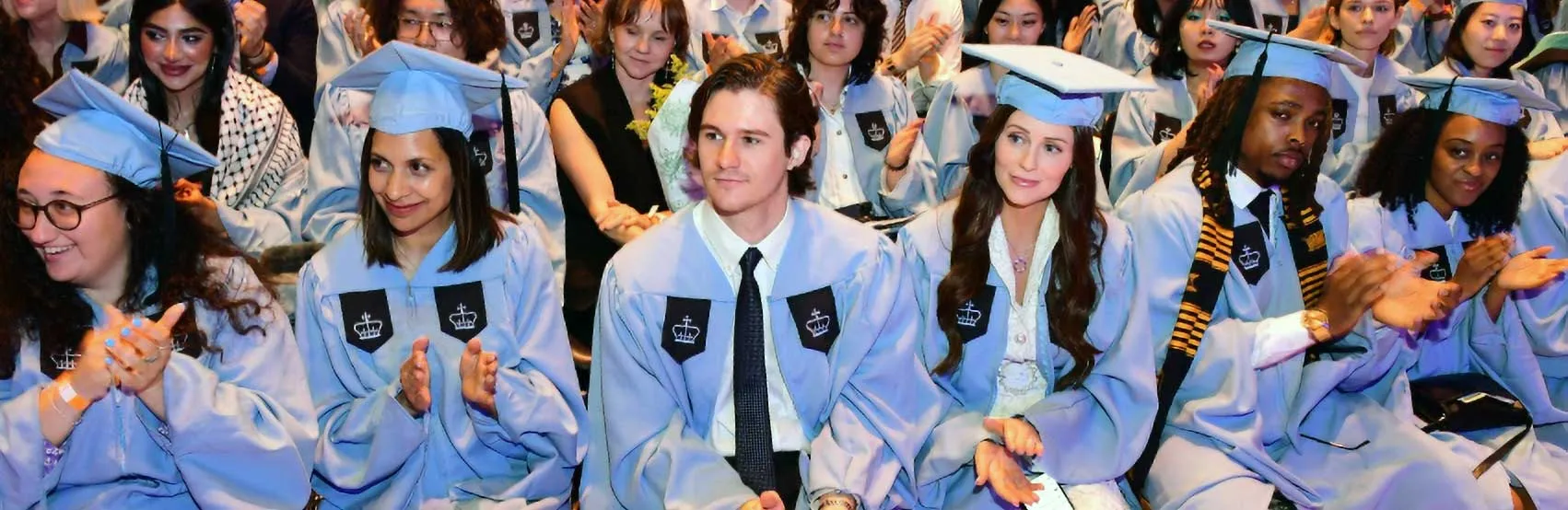 Graduates seated wearing Columbia blue caps and gowns during the Columbia Journalism School Class of 2024 graduation ceremony. 